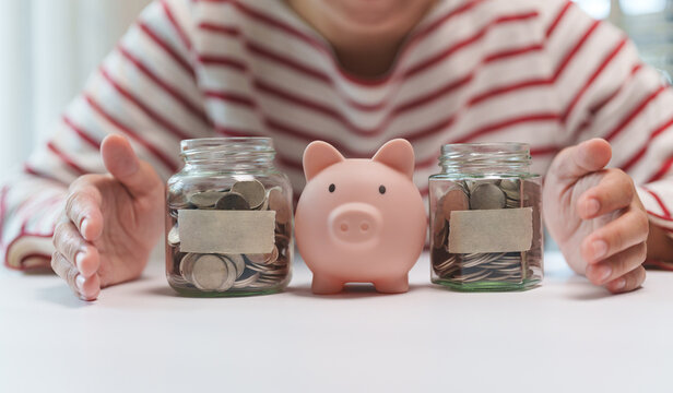 Asian woman organizing retirement savings with piggy bank and labeled coin jars to build long-term financial security and wealth.