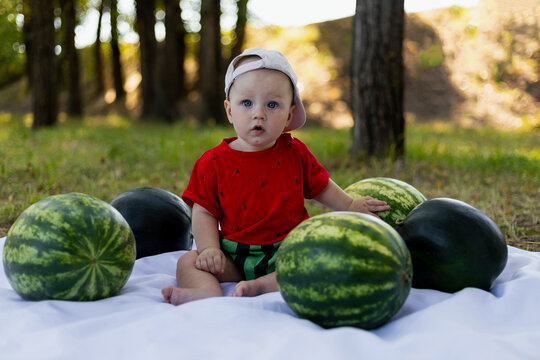 Cute baby in watermelon outfit surrounded by fresh watermelons in a park