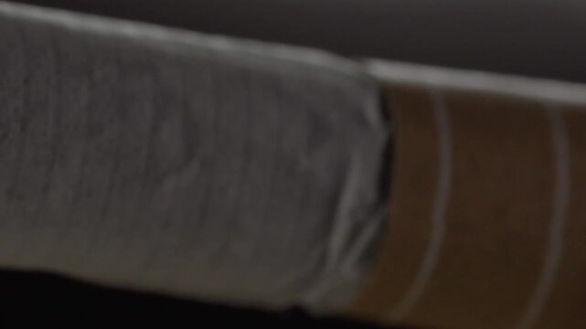 Close up panning shot moving along a hand rolled cigarette with exposed tobacco at one end. The textured paper and dark tobacco filling create detailed surface patterns.