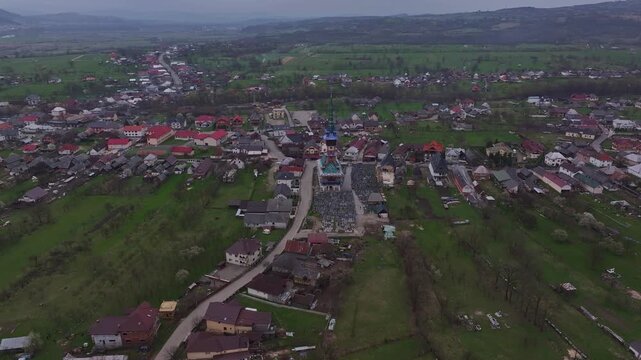 Aerial view of the rural landscape in Sapanta featuring green agricultural fields, traditional village houses, and a tall wooden church tower in Maramures, Romania.