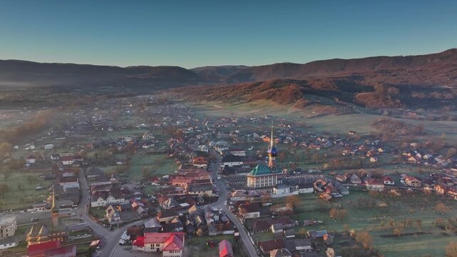 Drone shot of the rural village of Sapanta illuminated by golden sunrise light with thick morning mist in Maramures, Romania.