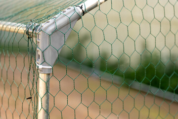 Close-up of green hexagonal chicken wire mesh attached to a galvanized metal frame, forming a protective poultry enclosure and fence for a backyard chicken coop. © Marek