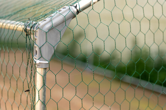 Close-up of green hexagonal chicken wire mesh attached to a galvanized metal frame, forming a protective poultry enclosure and fence for a backyard chicken coop.
