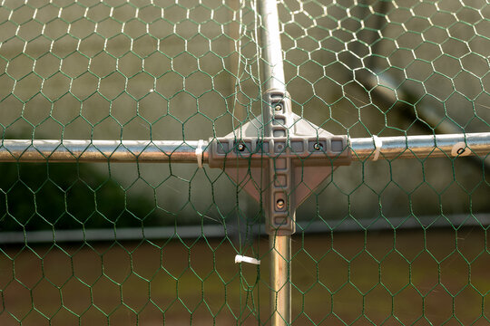 Close-up of green hexagonal chicken wire mesh attached to a galvanized metal frame, forming a protective poultry enclosure and fence for a backyard chicken coop.