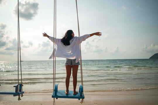 Happy woman celebrating freedom holding white shirt in the wind against blue sky at tropical beach