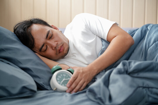 Man unshaven lay bed hold alarm clock. Man unshaven bearded wakeful face having rest. Stick schedule same bedtime wake up time. Enough sleep for him. Regulate your bodys clock. Sleep regime habit
