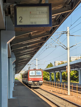 a train leaving an old station, with an analog split-flap railway departure board listing trains
