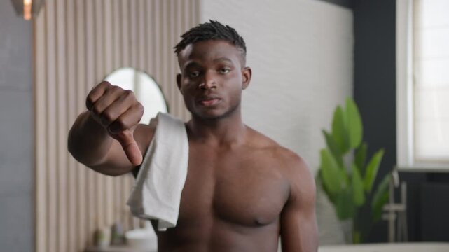 Sad African American man upset guy in bathroom showing thumb down gesture dissatisfied with bad result ethnic unhappy male model disagree dislike negative beauty cosmetics product indoors hotel bath