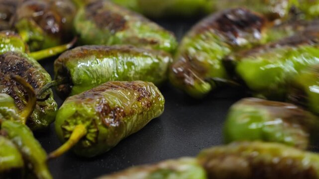 Green padron peppers frying in a pan, being stirred with a spatula.