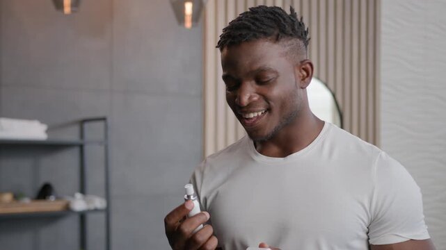 Smiling African American man applying fresh breath spray in bathroom preparing for date ethnic male guy morning hygiene of mouth prevent stink spraying freshener oral dental product refresh breathing