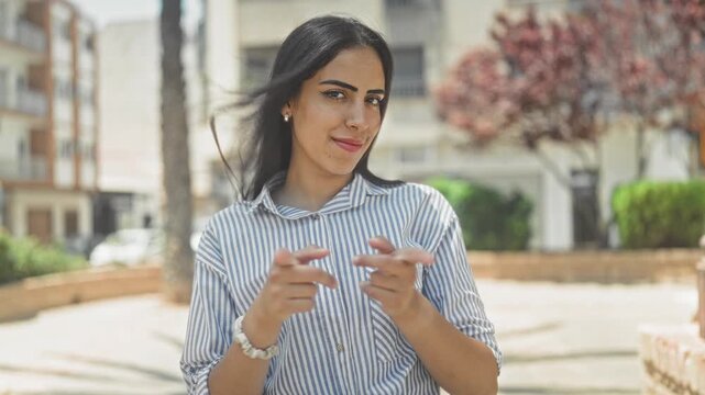 Woman forms heart with hands on street wearing striped blue shirt and bracelet; affection love connection.