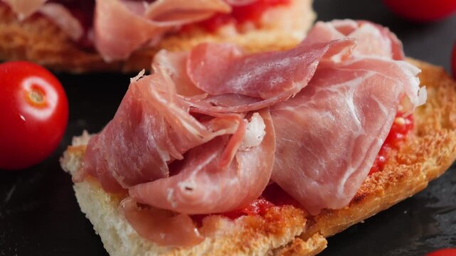 Toasted bread topped with grated tomato and slices of jamon, a traditional Spanish pan con tomate served with tapas.