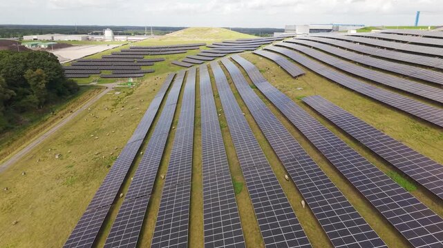 Aerial view of a solar park integrated with a waste management facility, featuring rows of solar panels on green fields with grazing sheep in Wijster, Drenthe, Netherlands.