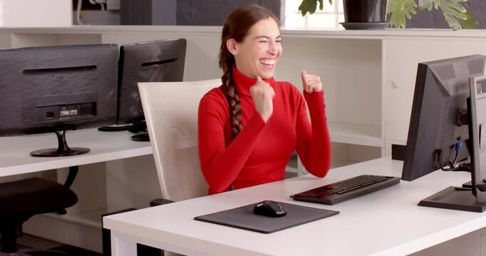 Woman in red sweater celebrating success at office desk with computer
