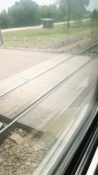 Parallel steel rails and concrete sleepers rush past an interior passenger window in daylight. Vertical framing offers authentic visual texture for travel narratives and reels.
