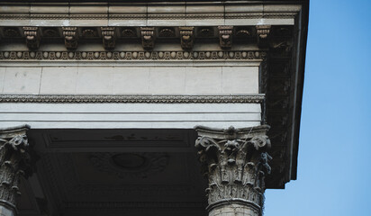 Architectural detail of classical stone building facade with Corinthian columns and ornate ornamental cornice against blue sky with copy space. © Вита Курило