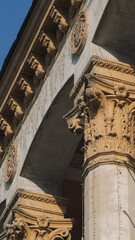 Low angle vertical view of classical building arch with ornate Corinthian capital, carved brackets, and decorative medallions bathed in warm sunlight. © Вита Курило