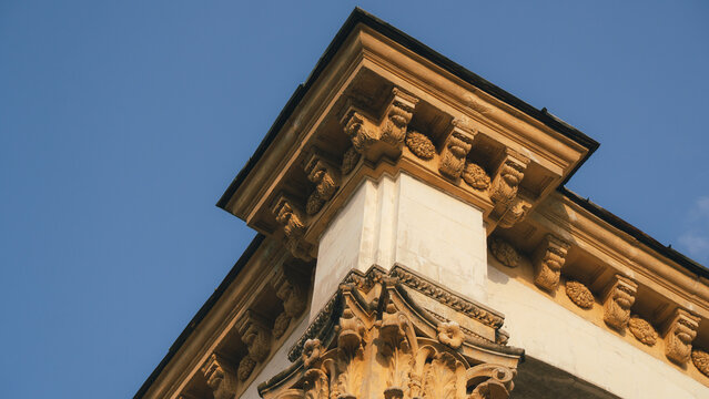 Low angle architectural view of classical stone building corner with ornate Corinthian capital and decorated cornice against blue sky