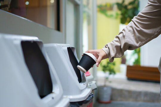 Person Disposing Disposable Coffee Cup into Trash Bin for Waste Management and Recycling