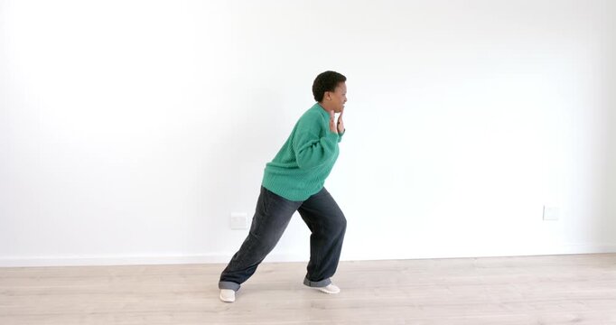 Person in green sweater energetically practicing dance moves in spacious room