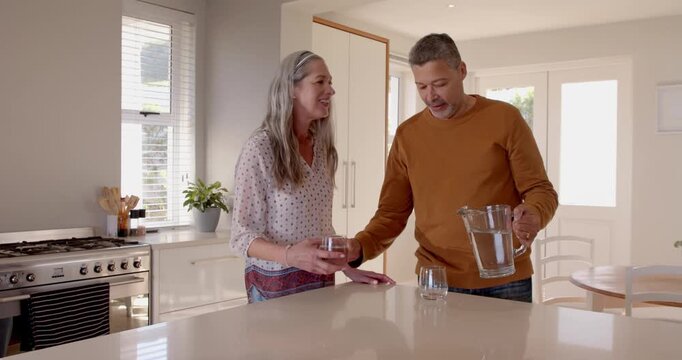 Happy senior couple in kitchen toasting with glasses of water, enjoying conversation