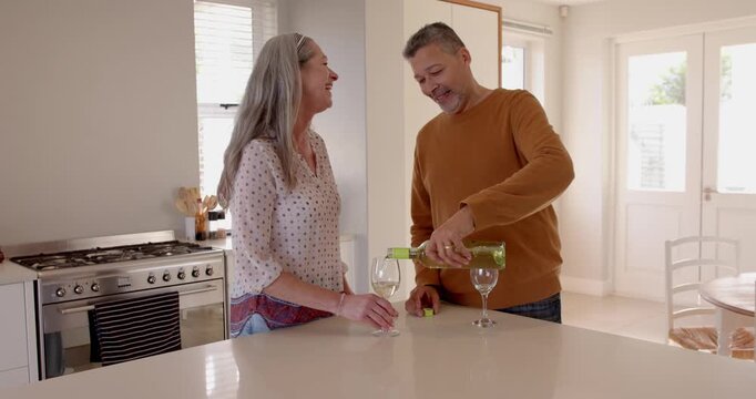Senior couple enjoying wine together in modern kitchen, smiling and toasting glasses