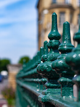 Close-up of decorative glossy green wrought-iron fence finials with blurred historic building behind