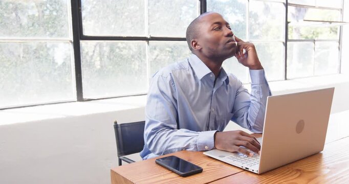 In office, businessman multitasking with smartphone and laptop, smiling confidently