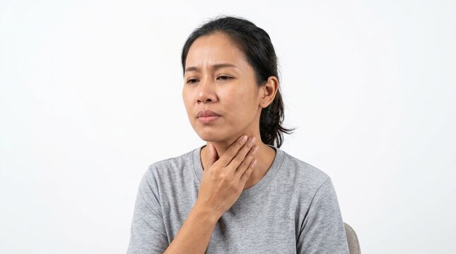Asian woman suffering from sore throat, touching her neck with painful expression, feeling sick with cold and flu symptoms, viral infection concept against a plain white background.