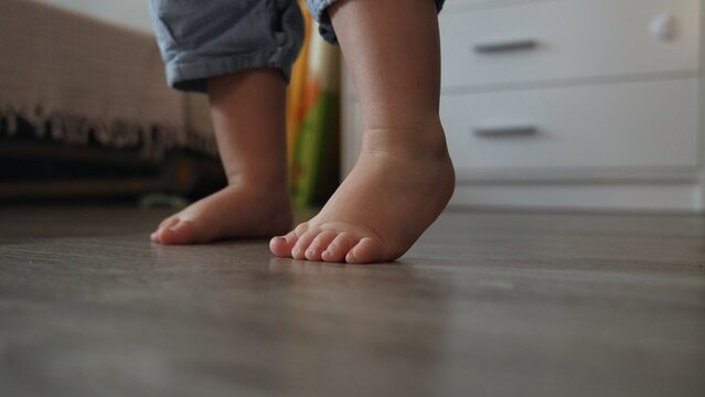 Close up of a toddler standing barefoot on a wooden floor in a bright home bedroom setting