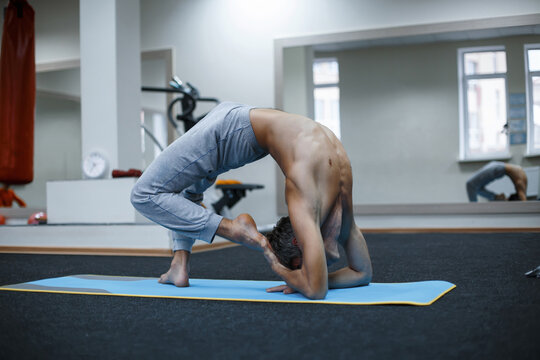 Athletic muscular young man working out, yoga, pilates, fitness training, doing side bend, asana Parighasana, Gate Yoga Pose in gym