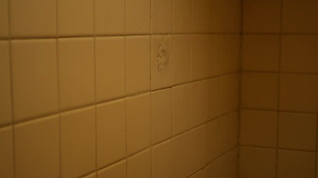 Angled View of Aged Bathroom Tile Corner with Warm Ambient Light and Worn Ceramic Surface