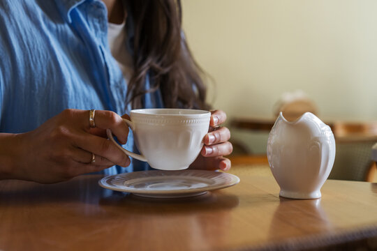 Close up of woman hands lifting white coffee cup from saucer