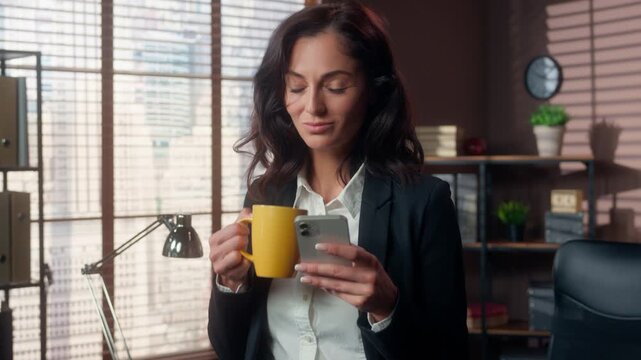 Smiling Caucasian business woman with coffee using mobile phone in office female businesswoman drinking cup browsing smartphone scrolling online social media manager work break employer girl inside