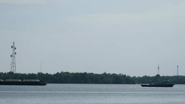 Colorful tugboat towing a small fishing boat with rope across calm blue sea, green navigation buoy and seagull on horizon