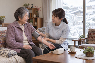 Fototapeta premium Home Care Nurse Measuring Blood Pressure of a Senior Japanese Woman in Winter 