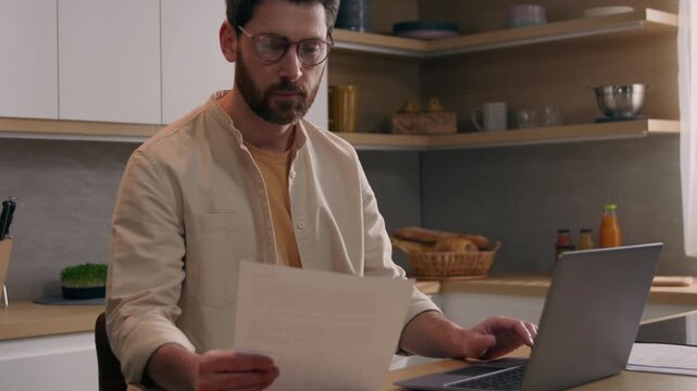 Serious Caucasian business man paying bills online laptop in kitchen busy businessman checking finances reviewing mortgage payments budget paperwork homeowner freelancer using banking website computer