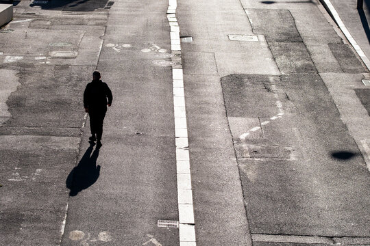 Solitary pedestrian walking along an empty urban roadway with a long shadow creating a minimalist city scene of movement solitude and public space