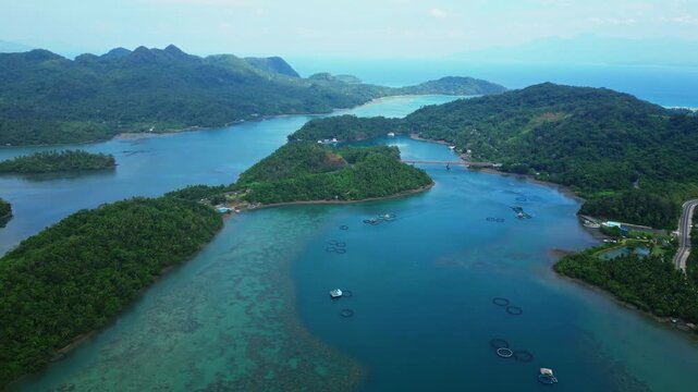 Drone perspective approaching Sula Bridge on Cagraray Island, Albay, with the surrounding tropical landscape and coastal waters extending toward the horizon under a cloudy sky.