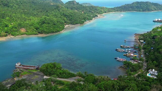 Aerial reveal from Sula Angling Spot on Cagraray Island, Albay, revealing vivid blue coastal waters and a wrecked tanker surrounded by the tropical island landscape.