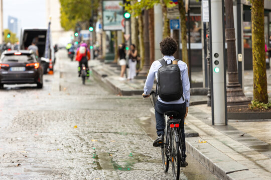Cyclist commuting through a busy city street after rain, sustainable urban transportation, active mobility, and everyday city life