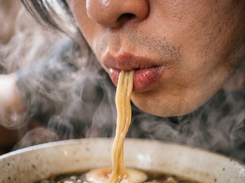Healthy eating brings joy. A person eagerly slurps hot wheat noodles from a steaming ceramic bowl of rich savory ramen broth.