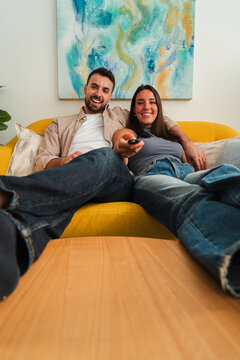 A cheerful couple lounges on a vivid yellow sofa, leaning back with relaxed smiles and warm companionship, captured for lifestyle home use and intimate everyday moments.