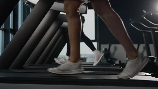 Close up multiethnic female male legs running on treadmill in fitness gym sports shoes couple cardio workout athletic runners jogging run machine muscular feet stride active lifestyle exercise indoors