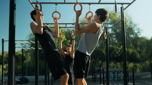 Youth team doing pull ups on the gymnastic rings at the outdoor sports ground.