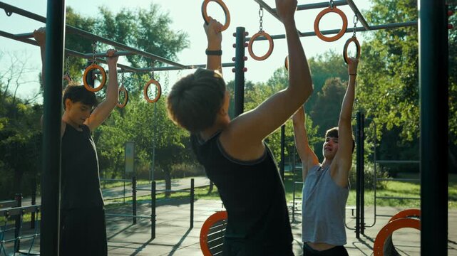 Teen youth group doing pull ups on gymnastic rings during outdoor training.