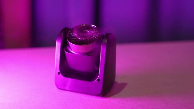 Close-up of a modern black aroma diffuser emitting a gentle mist indoors. The sleek electronic device rests on a clean surface, illuminated by vibrant purple and pink neon studio lighting.