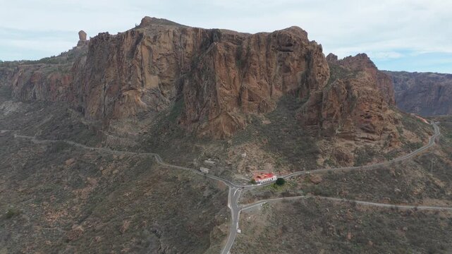 Aerial drone pull back shot revealing a breathtaking view of a rugged volcanic mountain landscape and winding roads on Gran Canaria. Showcases the island's unique and remote natural beauty.