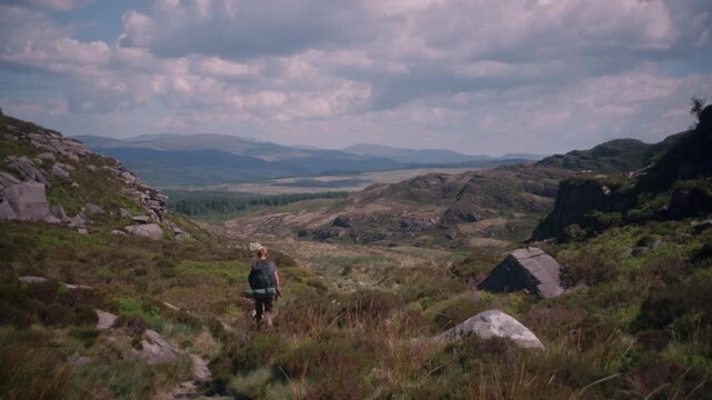 A rocky gully path winds through green gorse shrubs on the mountain trail, framed by rugged terrain.