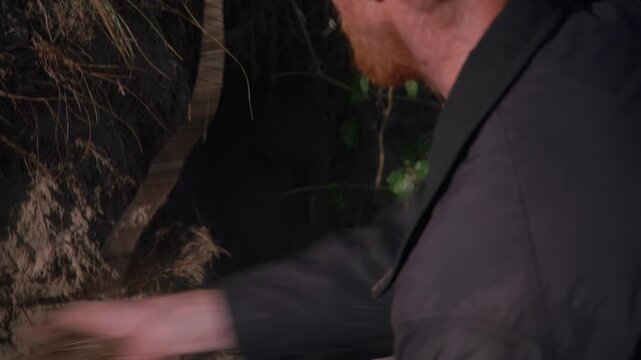 Close-up of hands rummaging in a dug pit in the sand, surrounded by dune grass, part of the camp preparation routine.